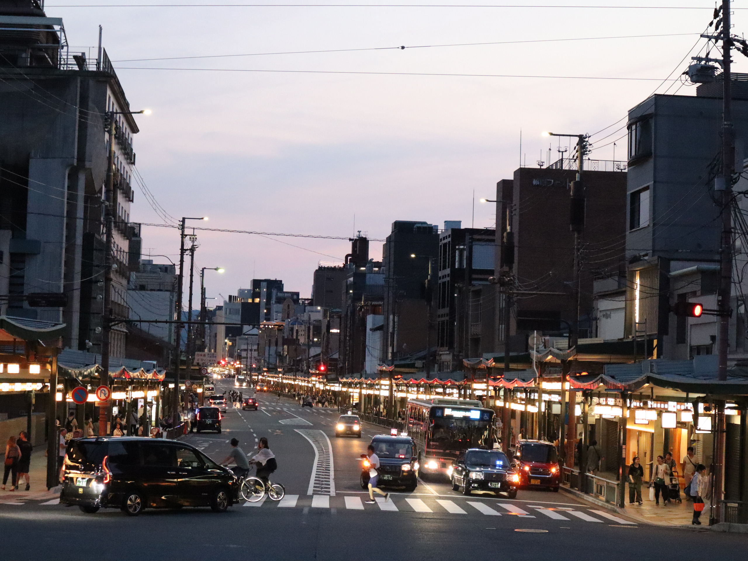暮色中的祇园街道，沿街店铺亮灯，车辆与行人来往