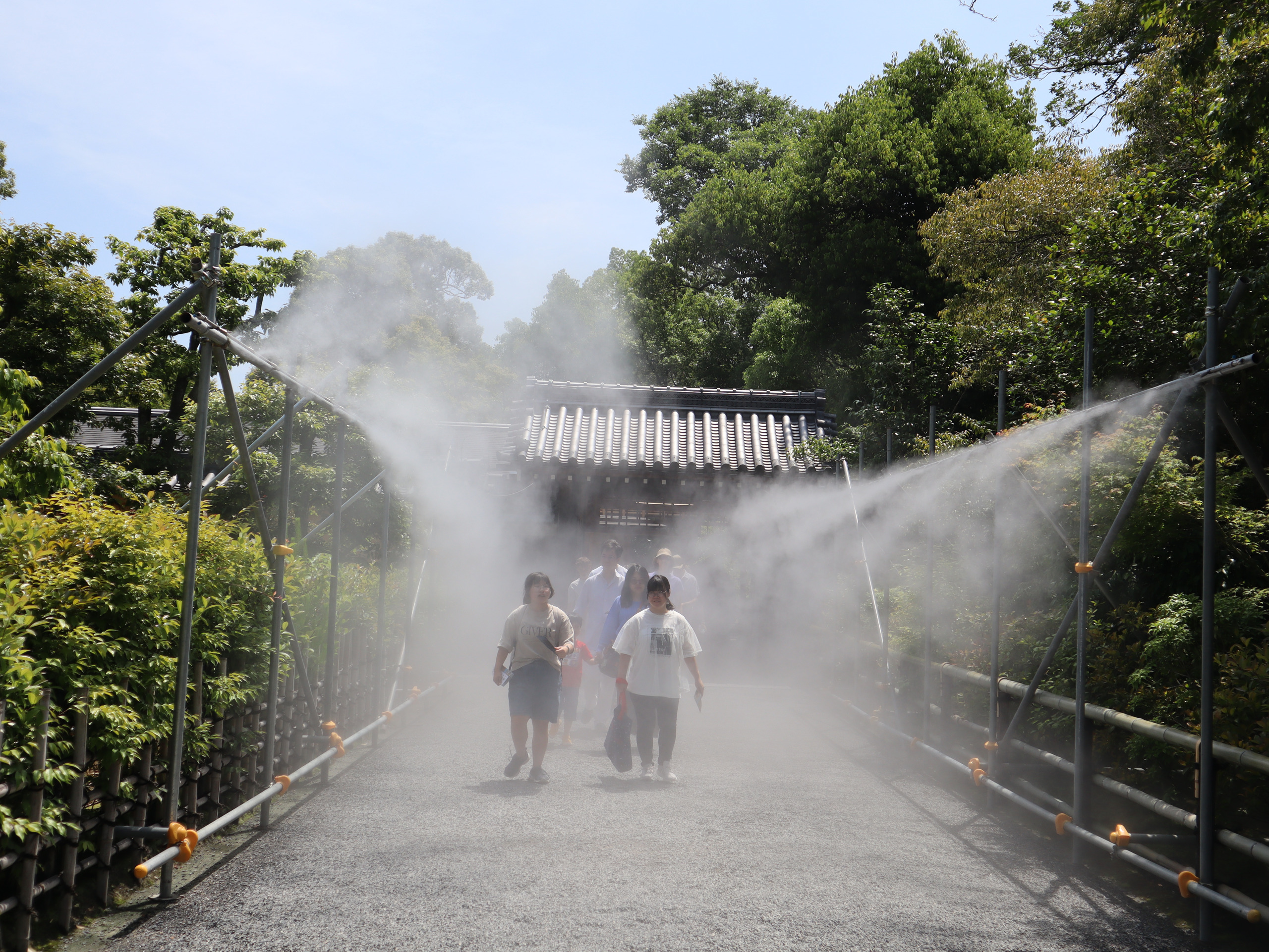 金阁寺入口附近的水雾，行人走过绿树夹着的道路