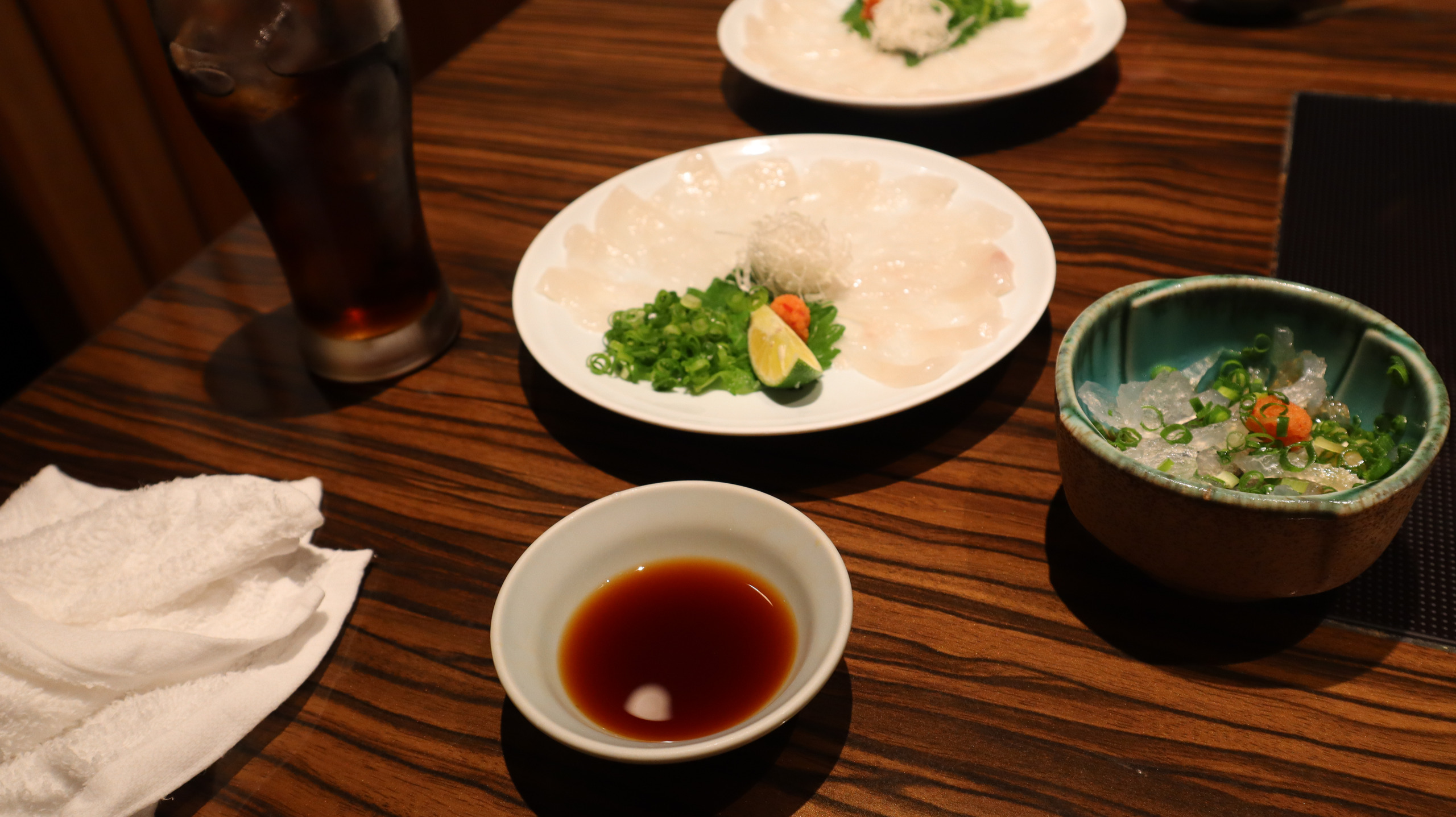 玄品餐桌上沿白盘排开的薄鱼片,配葱花、柑橘与蘸汁