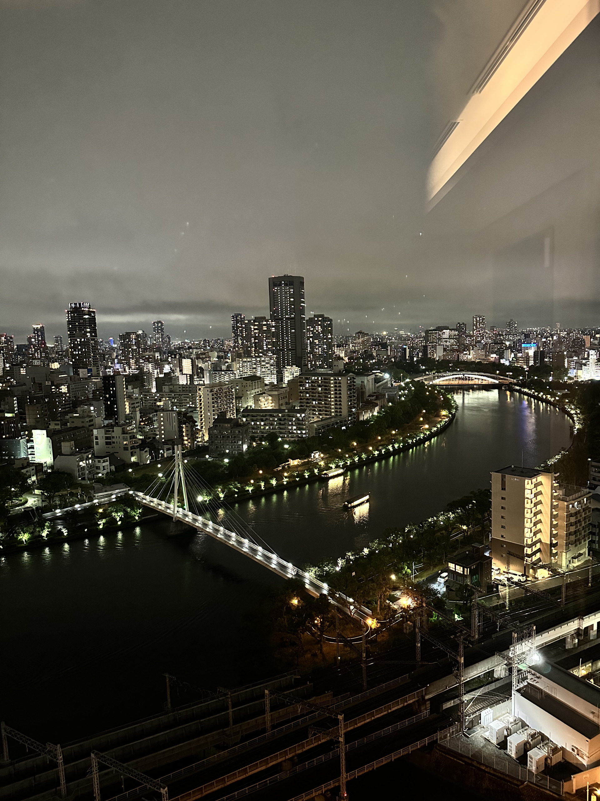 隔窗俯瞰大阪夜间河道与桥梁,玻璃上映着室内的暖色灯带