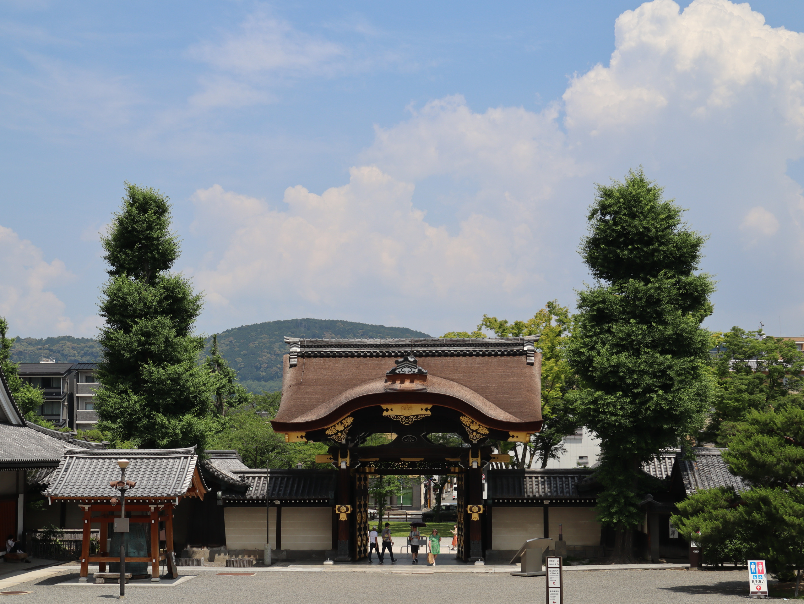 东本愿寺的阿弥陀堂门，两侧高树与远山映在蓝天白云下