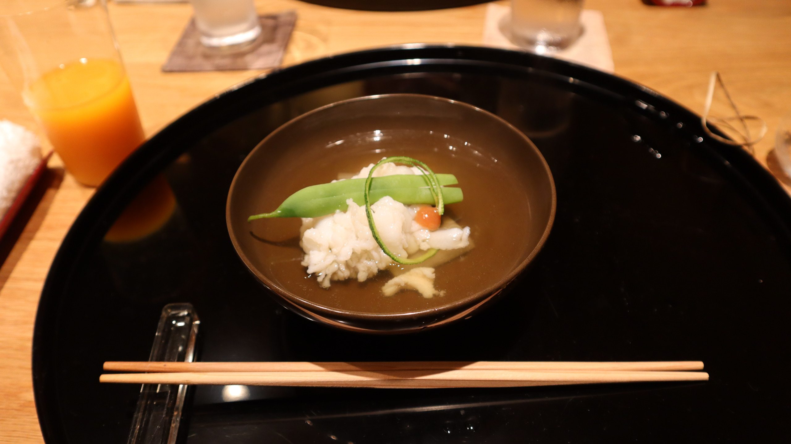 深色漆碗中的清汤,浅色食材上点缀着绿色与橙色