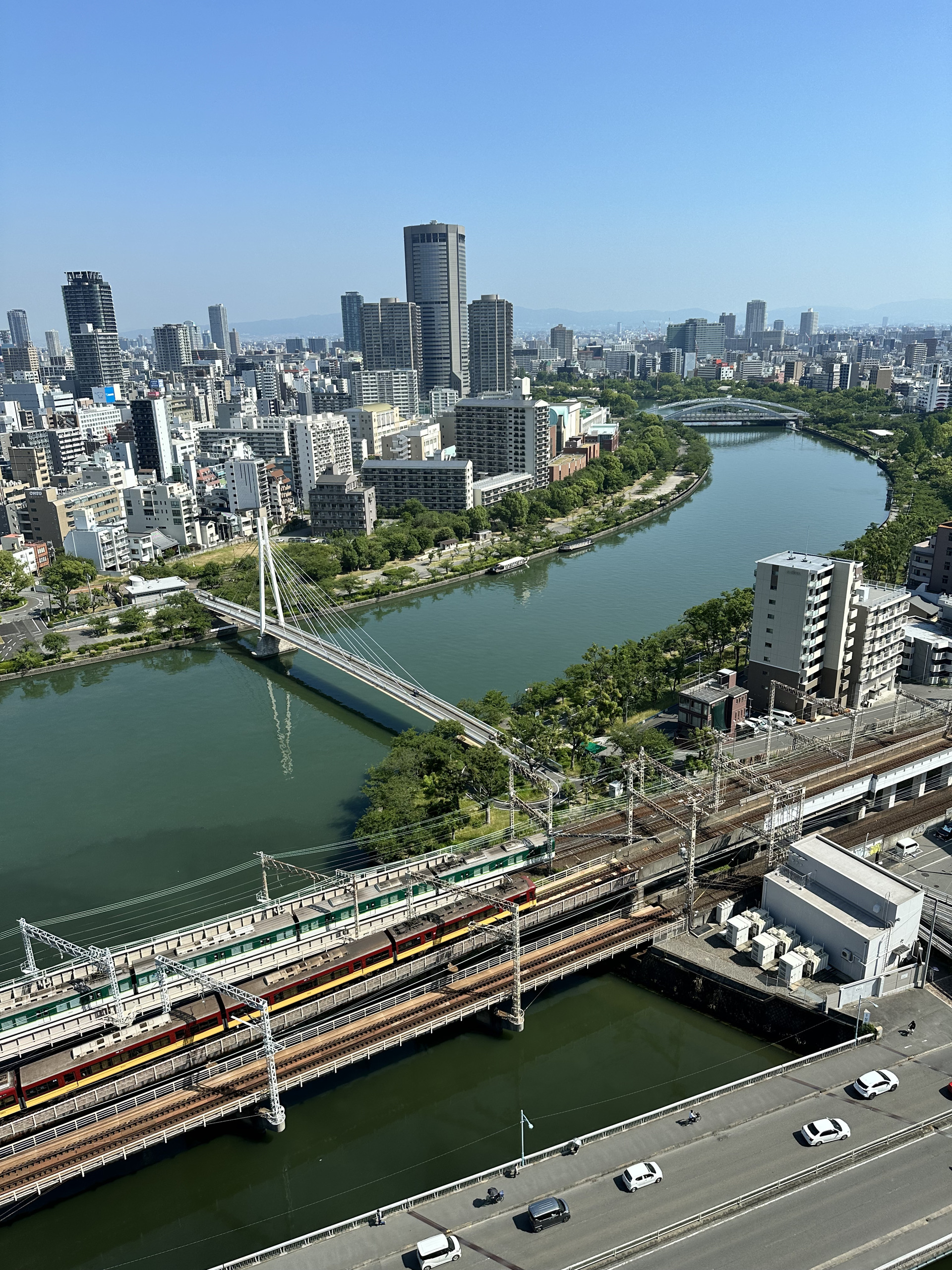 从大阪高处望向河道、铁路桥与楼群,列车正经过桥面
