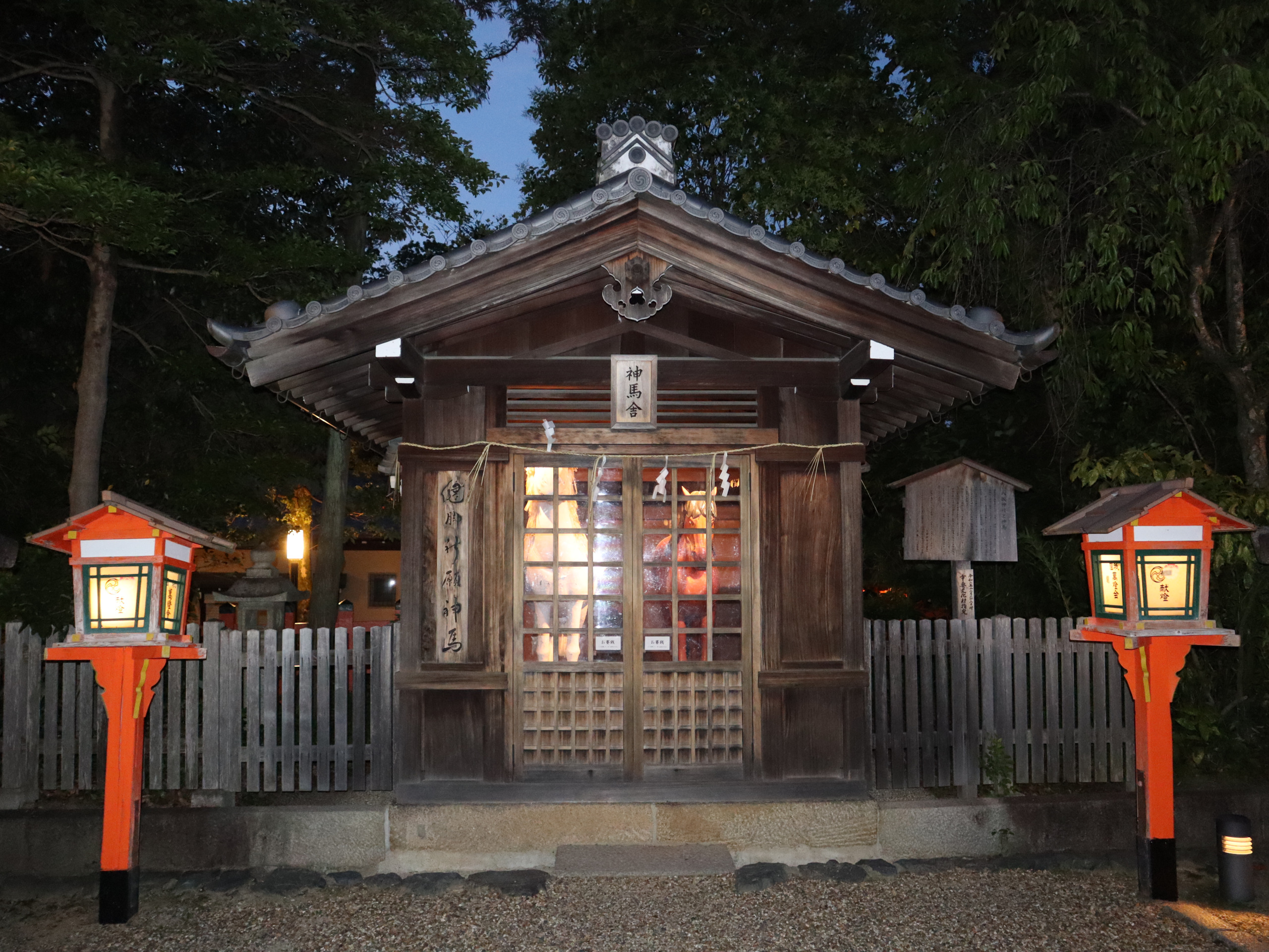 八坂神社境内的小社，木门内透出暖光，两旁立着红色灯笼